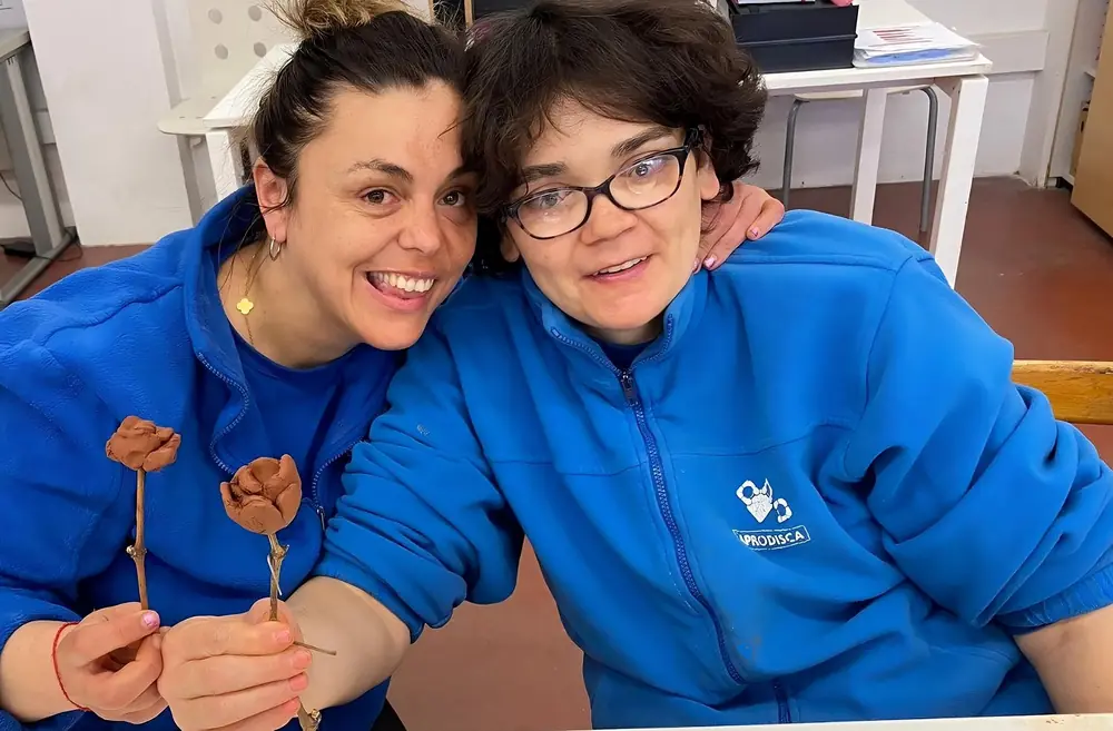 Dues persones amb el polo d'APRODISCA, somrient, amb roses fetes de fang a les mans